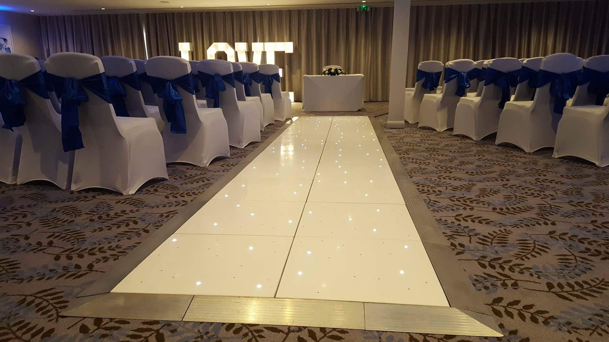 White starlit dancefloor used as an aisle with chairs with bows either side