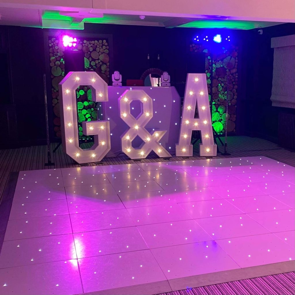 White starlit dance floor in front of giant light up letters and DJ