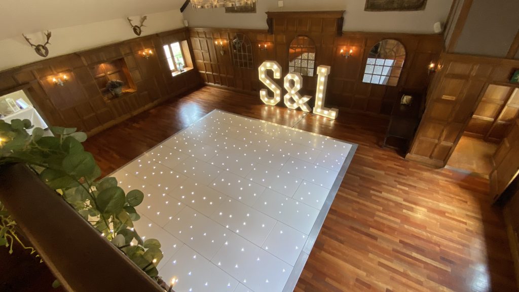 Top view of a led twinkle white starlit dance floor in a room with wood panels on the walls and wooden flooring. 