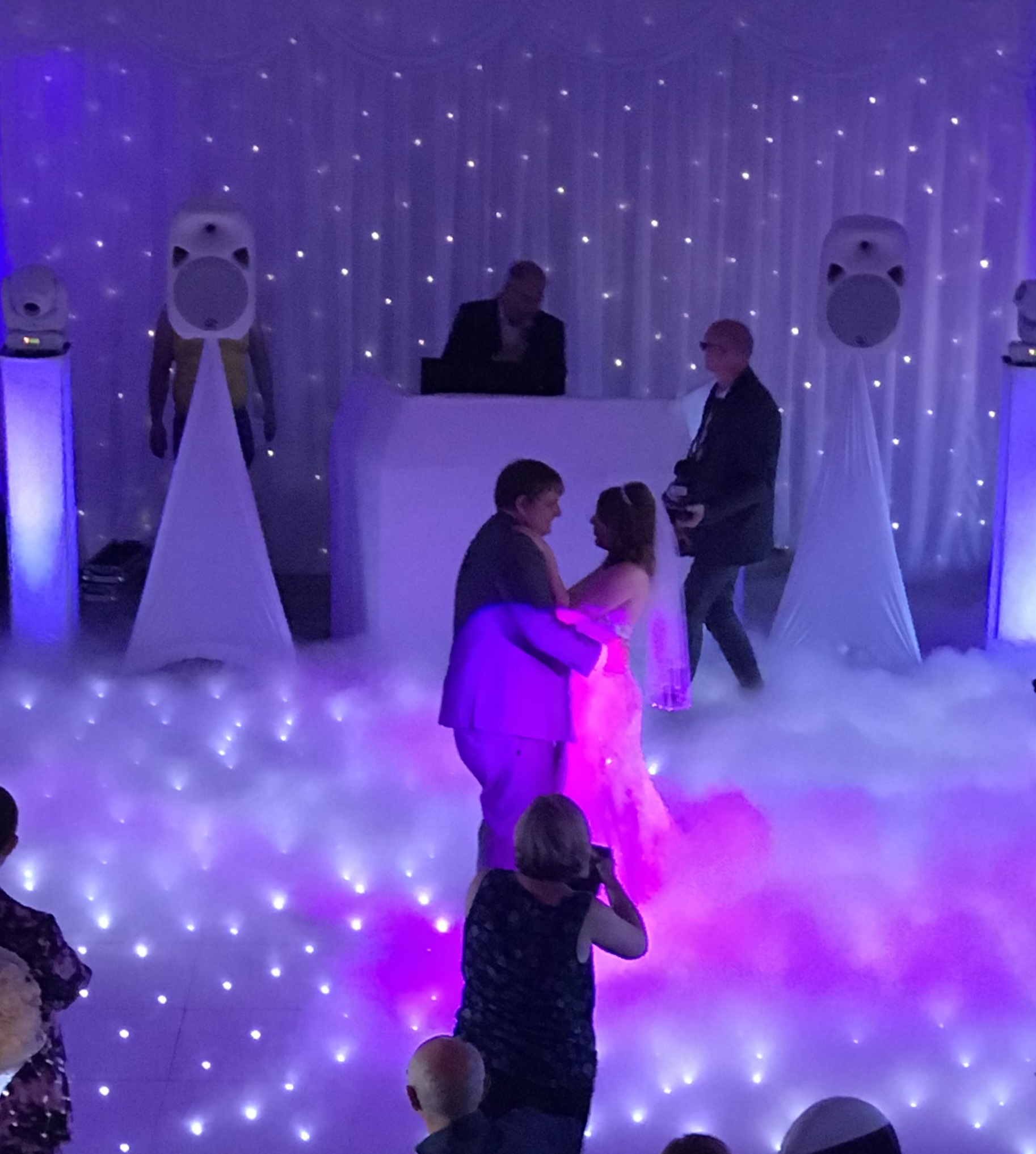 Couple on a white starlit dance floor with a disco set in white and dry ice giving the effect of dancing on clouds.
