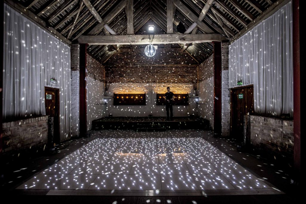 A white starlit dance floor setup in a rustic barn