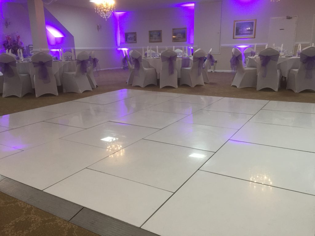 Pure white dance floor setup in amongst tables with purple backlighting. 