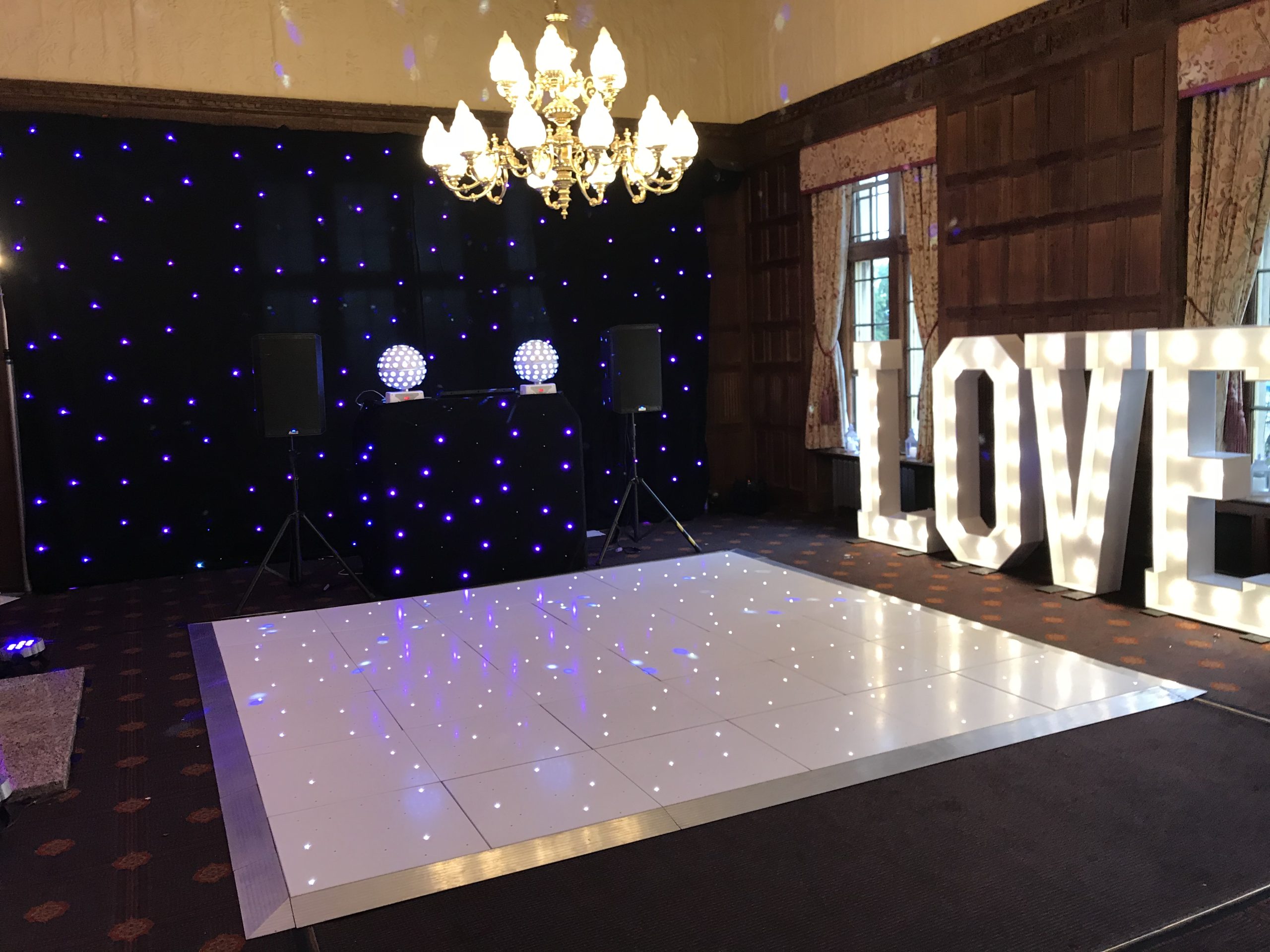 White led twinkle dance floor with large light up LOVE letters with a DJ setup and black starcloth backdrop.