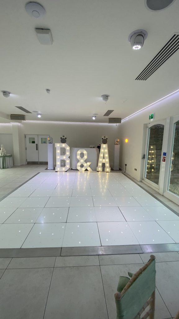 LED Twinkle dance floor in white with DJ setup and light up letters behind. No one is on the dance floor