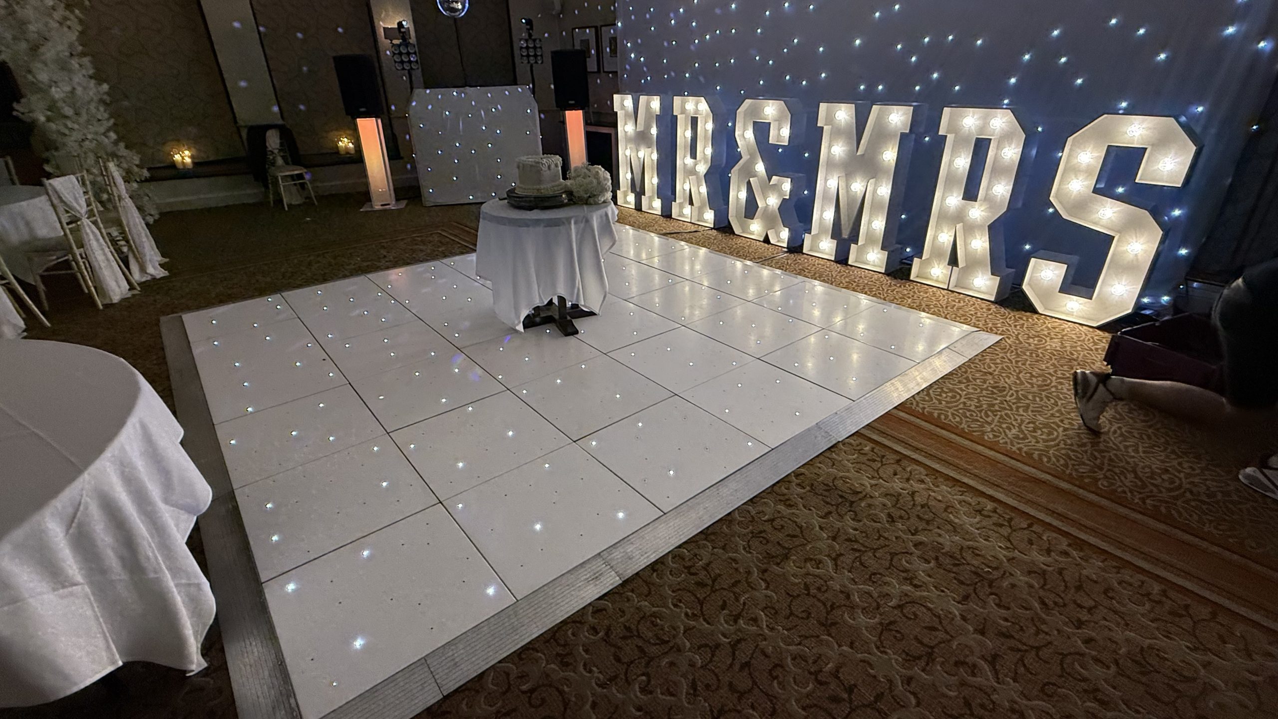 White starlit dance floorwith MR & MR letters behind and a wedding cake on the dance floor