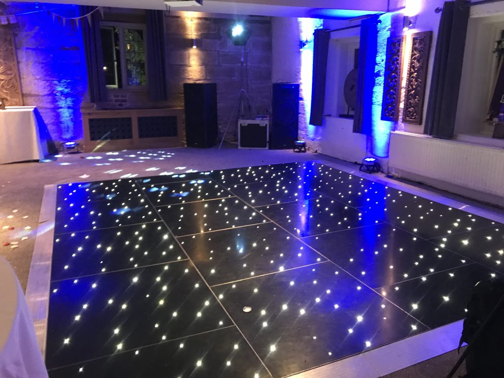 Black starlit led dance floor with blue lighting behind a dj booth